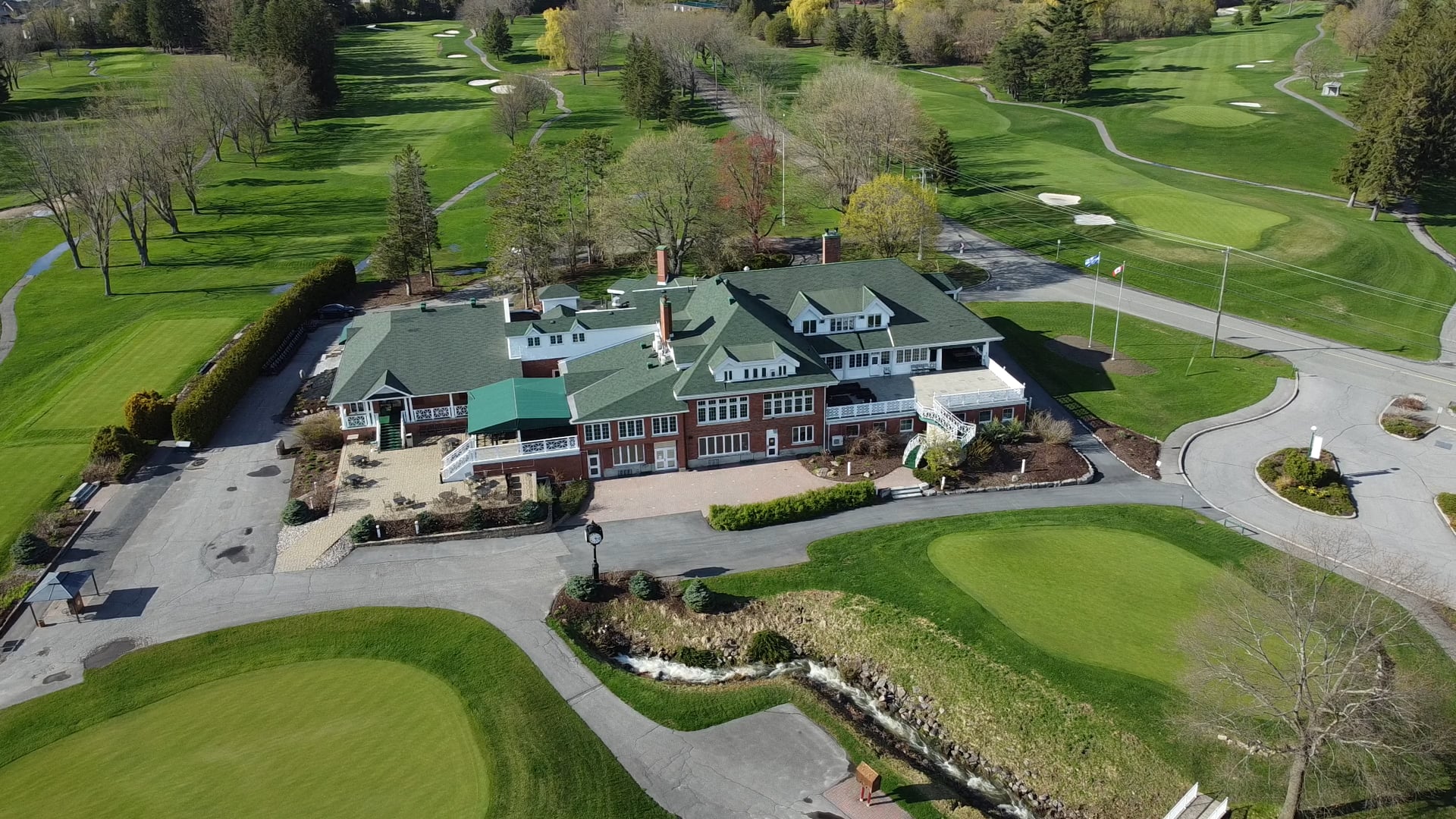 Aerial view of Rivermead's red-brick clubhouse under its green roof, fairways and the putting green on every side