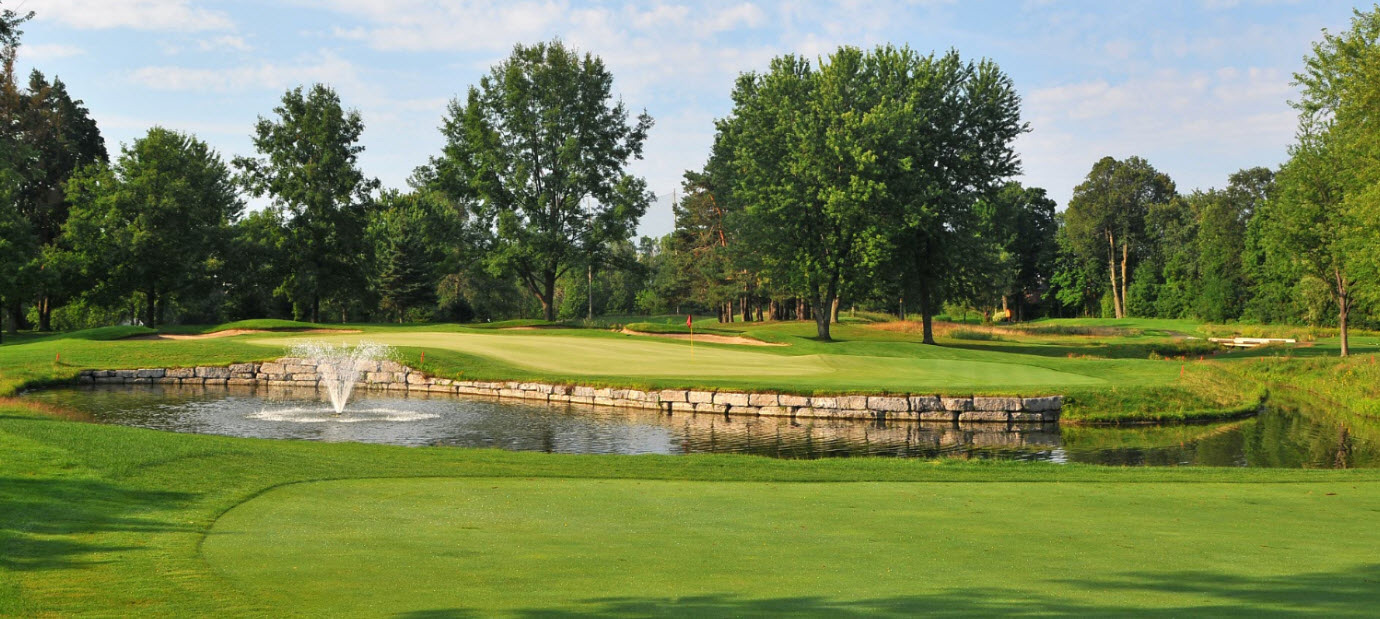 The eighteenth green behind its stone-walled pond and fountain on a summer morning