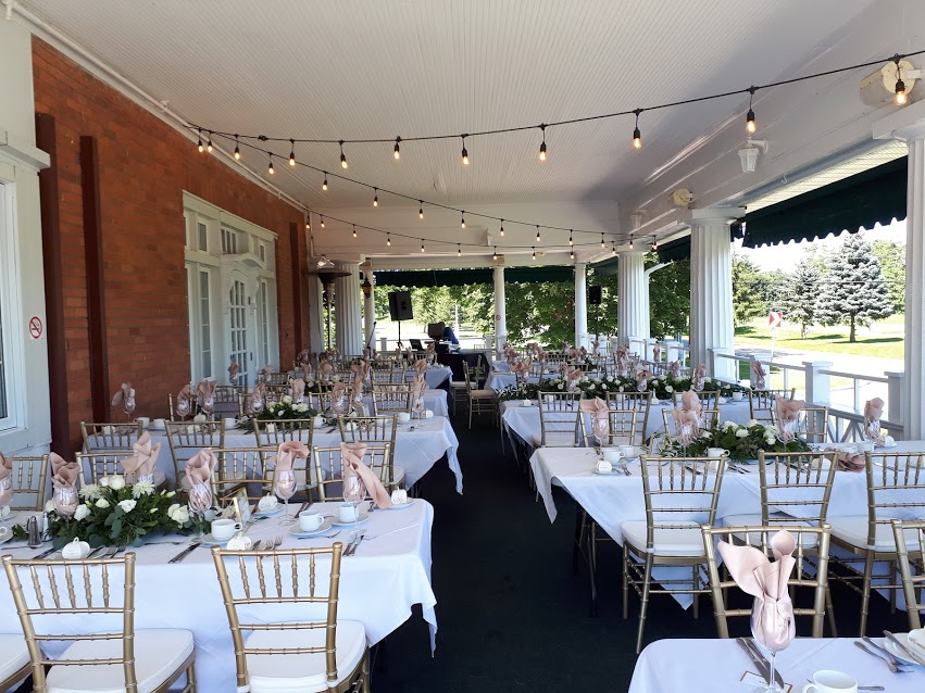 The covered veranda set for a dinner, string lights strung between white columns
