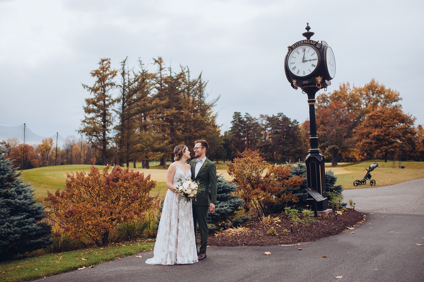 Newlyweds beside the Rivermead clock, its face marked 1910, with autumn colour behind