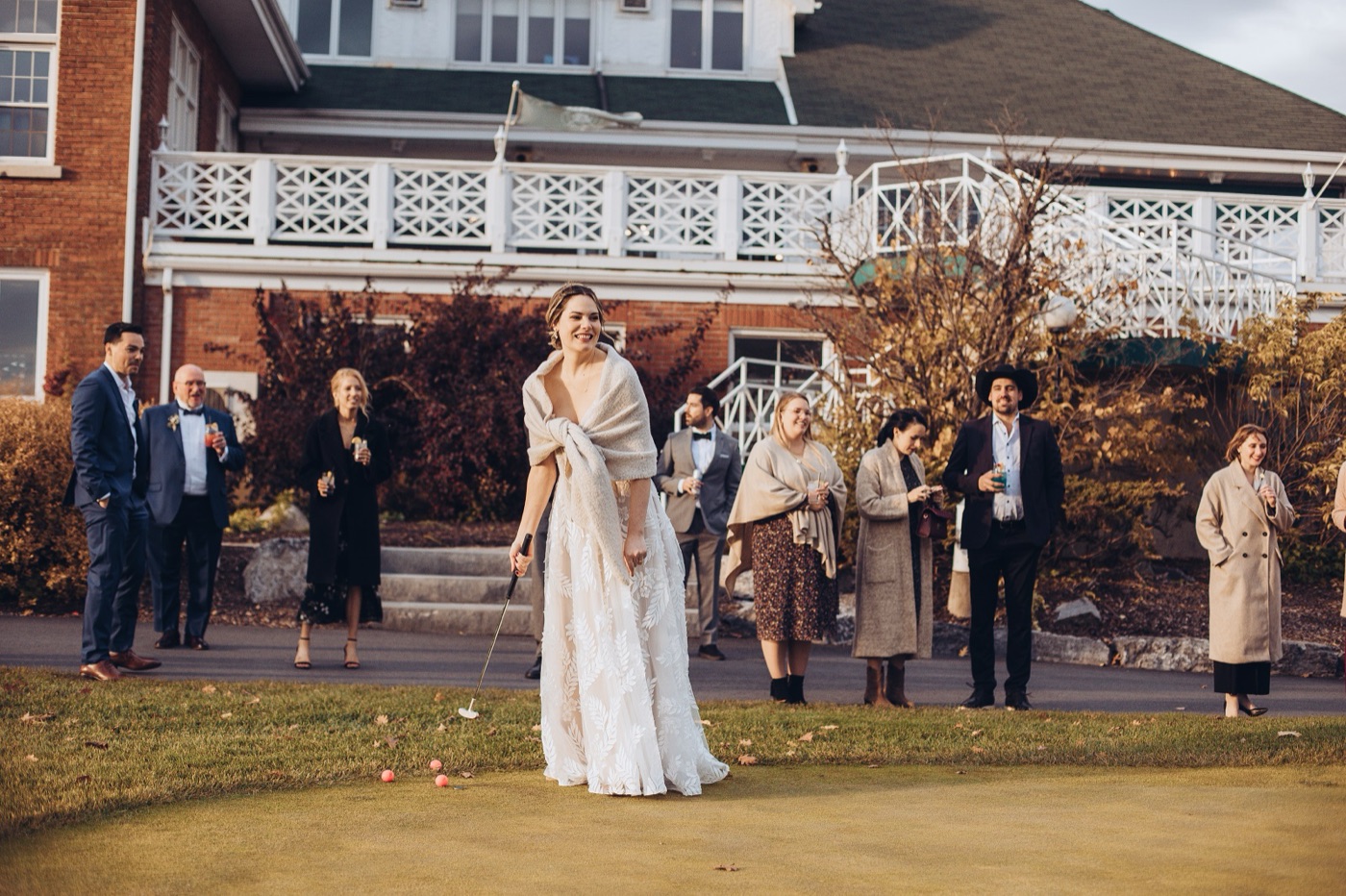 A bride putting on the green in front of the clubhouse while wedding guests look on