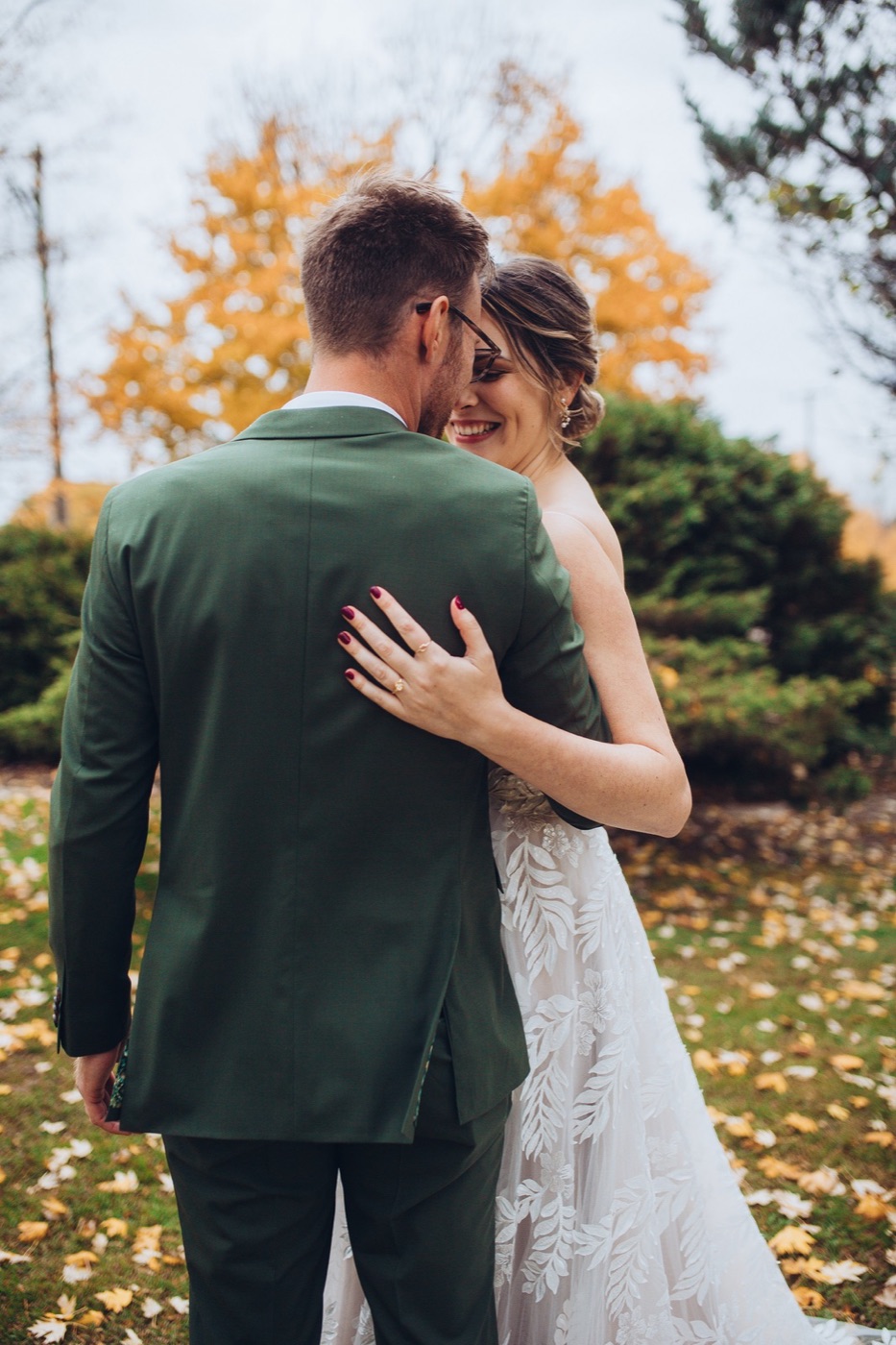 A couple embracing among autumn maples, the bride's hand on the groom's green jacket